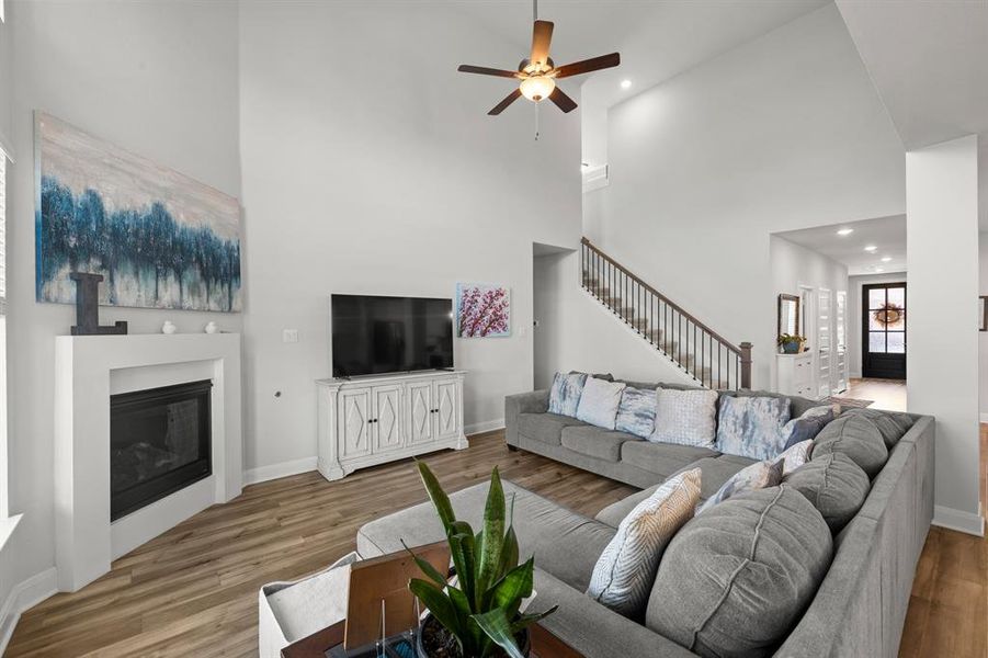Living area featuring a towering ceiling, wood finished floors, ceiling fan, a glass covered fireplace, and stairs Living area featuring a towering ceiling, wood finished floors, ceiling fan, a glass covered fireplace, and stairs
