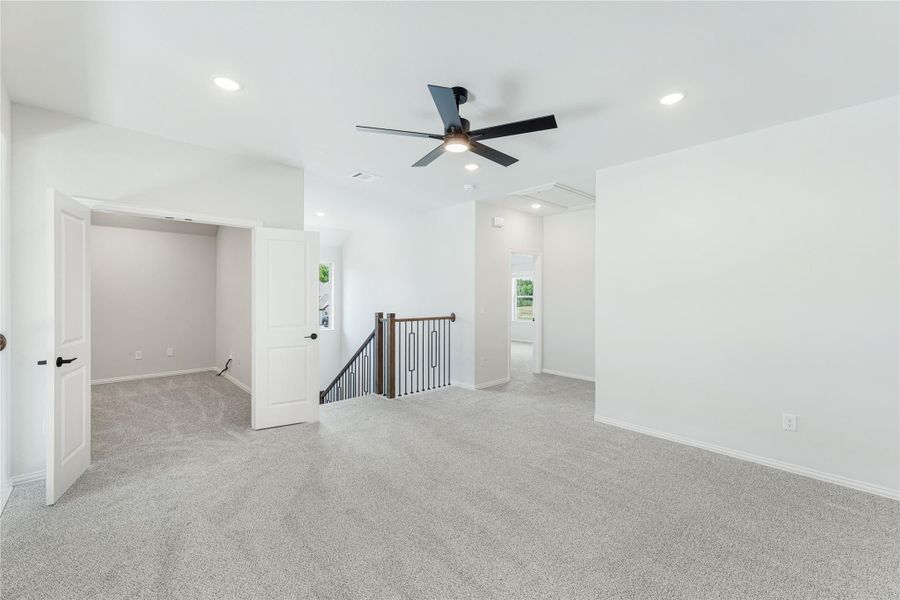 Open upstairs loft area with carpet, black ceiling fan, staircase railing, and recessed lighting