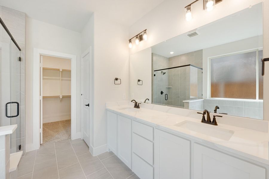 Bathroom with double vanity, white cabinets, glass shower, and walk-in closet entrance