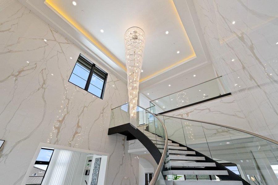 A grand entrance with a dazzling multi-tiered chandelier illuminates a sleek curved staircase and polished walls.