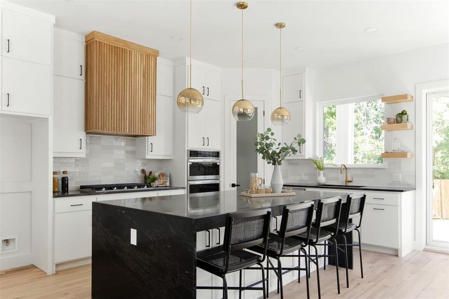 Kitchen with wall chimney range hood, light hardwood / wood-style floors, a kitchen island, and backsplash