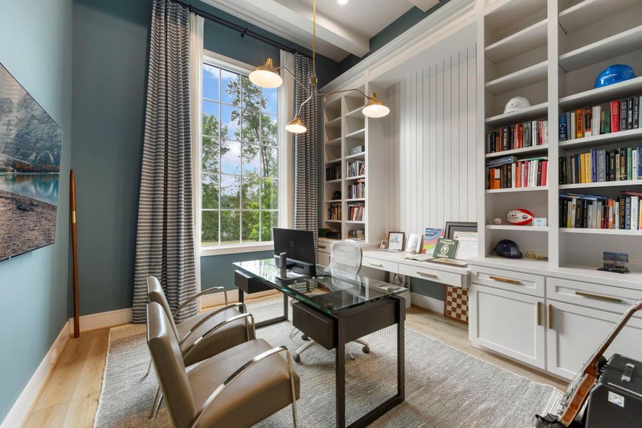 Sophisticated home office with custom built-in shelving, tailored cabinetry, and a statement chandelier, complemented by a large window that frames serene outdoor views and fills the space with natural light.