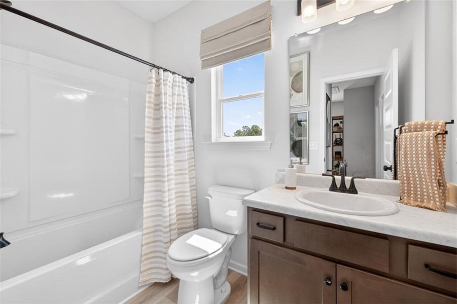 Full bathroom featuring a white tub/shower combination, dark wood-finish vanity with a light countertop, integrated sink, and a large mirror with overhead lighting