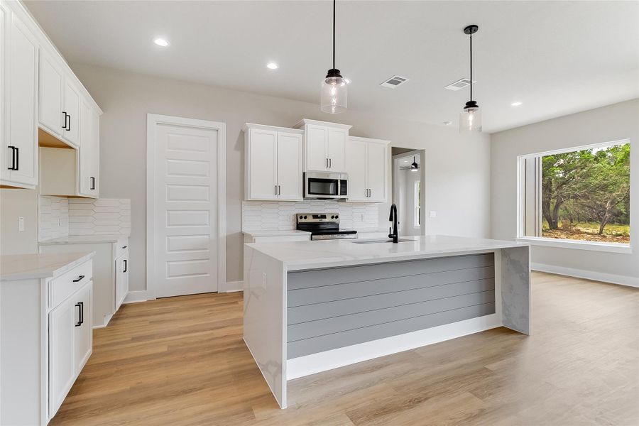 Modern kitchen featuring large center island with waterfall-style quartz countertops, large pantry, modern fixtures, and sleek cabinetry Modern kitchen featuring large center island with waterfall-style quartz countertops, large pantry, modern fixtures, and sleek cabinetry