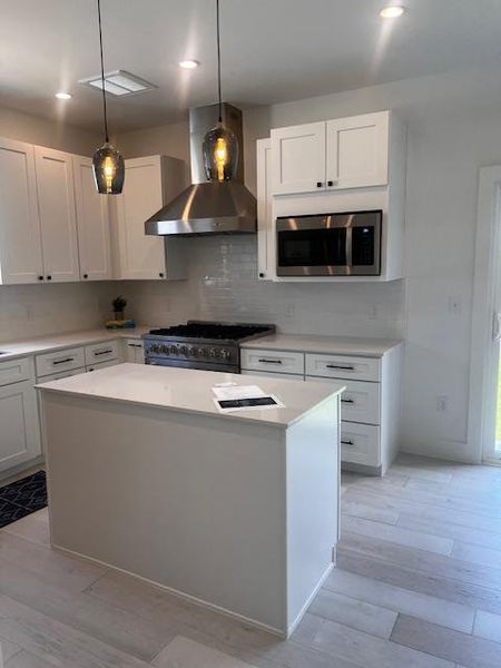 Kitchen with range hood, stove, a kitchen island, light countertops, and decorative backsplash