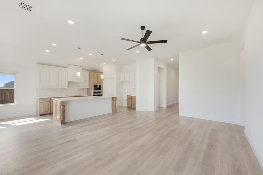 Open-concept living area with kitchen island, white cabinets, light wood floors, and ceiling fan