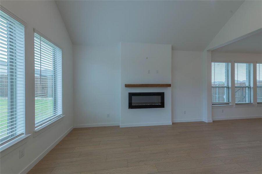 Unfurnished room with light carpet, vaulted ceiling, plenty of natural light, and baseboards