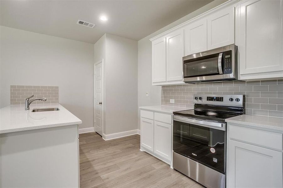 Kitchen featuring white cabinetry, decorative backsplash, stainless steel appliances, a peninsula, and light wood-style floors