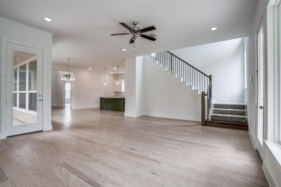 Unfurnished living room with light wood-type flooring and ceiling fan with notable chandelier