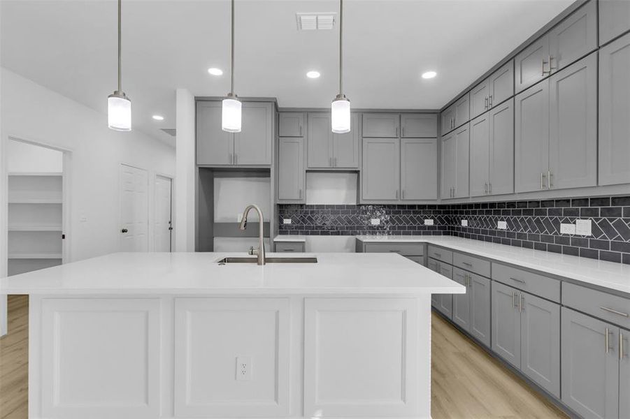 Kitchen with gray cabinetry, light stone counters, tasteful backsplash, hanging light fixtures, and light wood-style flooring