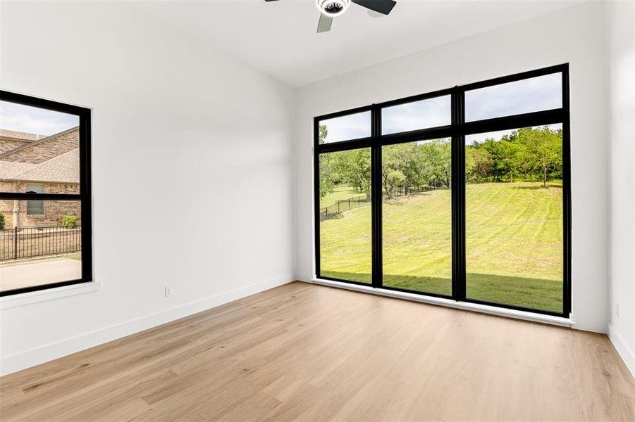 Expansive window wall with black framing, wood-finish flooring, crisp white walls, and a ceiling fan