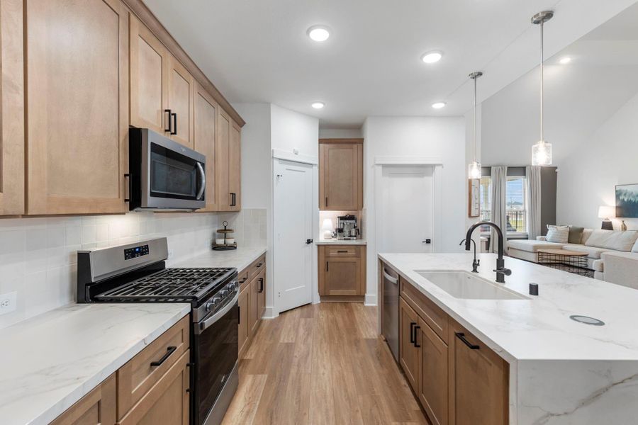 This modern kitchen features sleek wood cabinets, stainless steel appliances, and a spacious marble countertop island with a built-in sink. The open layout flows into a cozy living area, enhanced by pendant lighting and natural light from large windows. This modern kitchen features sleek wood cabinets, stainless steel appliances, and a spacious marble countertop island with a built-in sink. The open layout flows into a cozy living area, enhanced by pendant lighting and natural light from large windows.