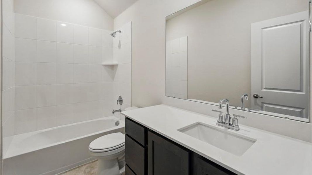 Contemporary bathroom featuring a dark wood-finish vanity with a white countertop and integrated sink, a large wall-mounted mirror, and a white tiled shower/tub combination
