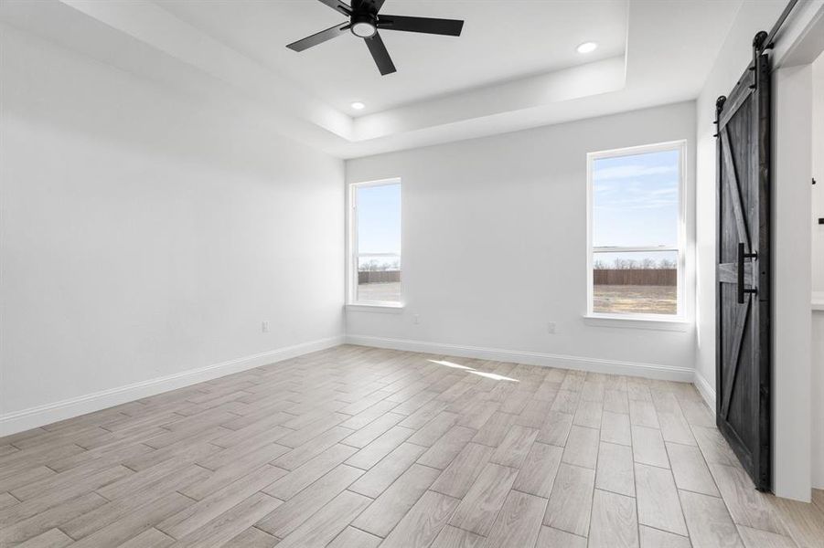 Unfurnished room featuring ceiling fan, a tray ceiling, a barn door, and light hardwood / wood-style floors