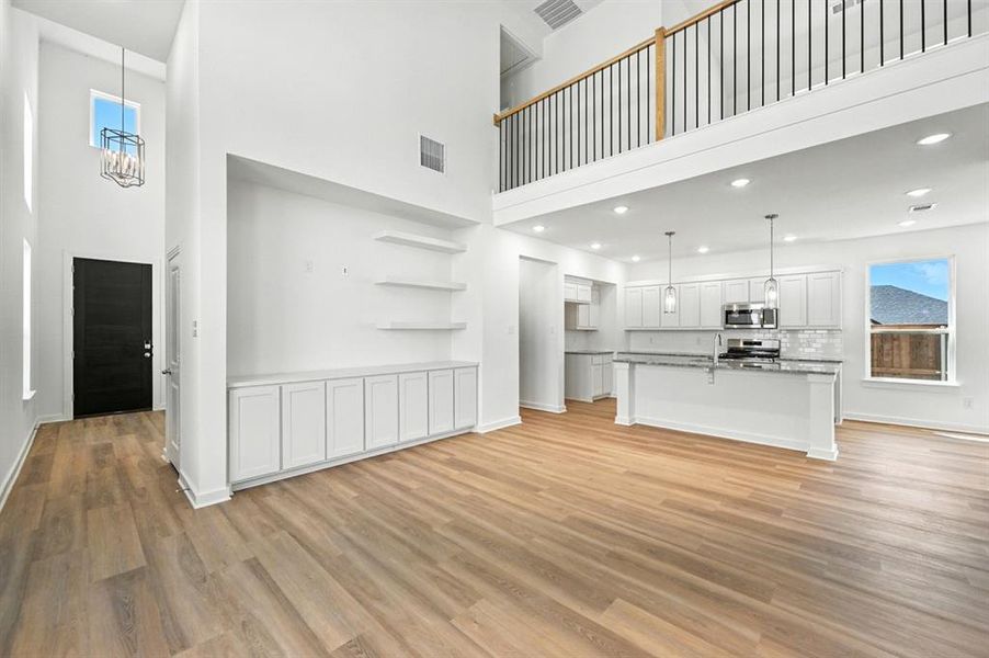 Unfurnished living room with light wood-type flooring, a towering ceiling, and recessed lighting