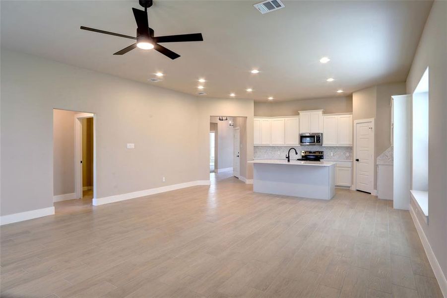 Kitchen featuring open floor plan, white cabinets, a kitchen island with sink, light wood-style flooring, and recessed lighting Kitchen featuring open floor plan, white cabinets, a kitchen island with sink, light wood-style flooring, and recessed lighting