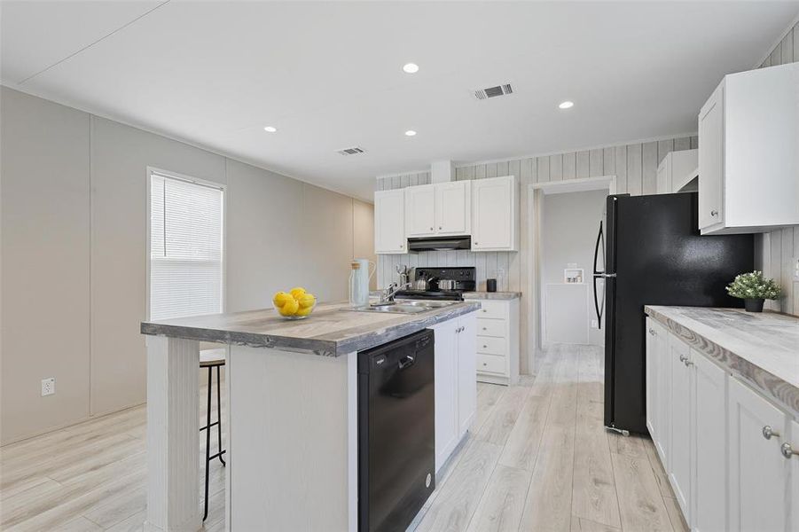Kitchen with white cabinets, a center island with sink, black appliances, light countertops, and recessed lighting Kitchen with white cabinets, a center island with sink, black appliances, light countertops, and recessed lighting