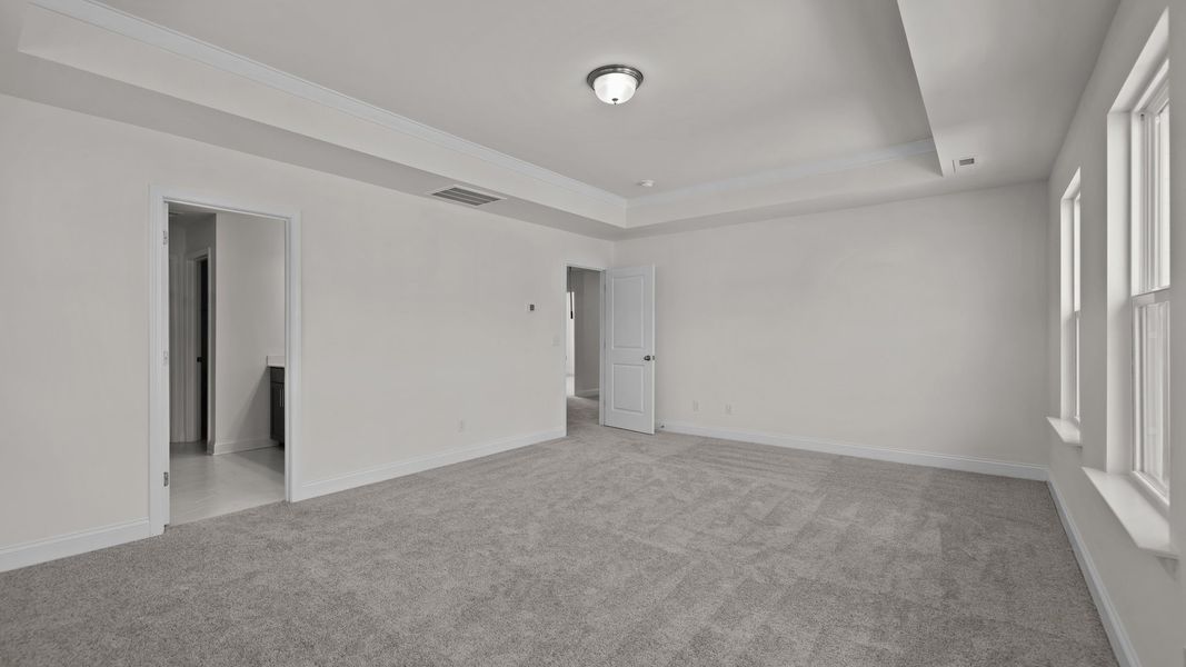 Burton Design oversized primary bedroom with raised tray ceiling and large windows. By DRB Homes at Lakeside Glen in York, SC