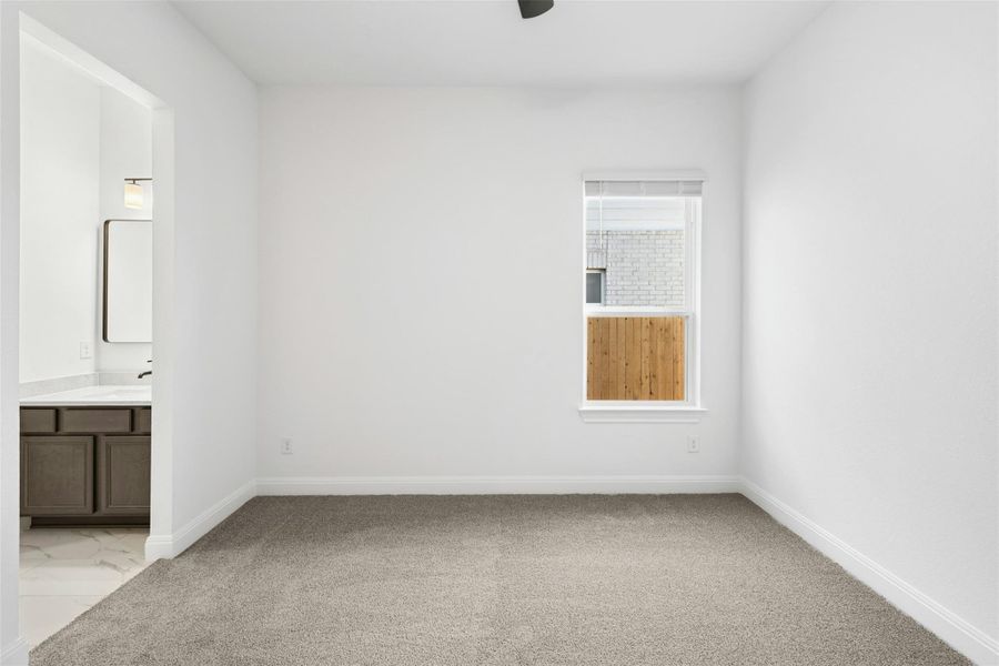 Unfurnished bedroom featuring ensuite bath, light colored carpet, and a ceiling fan