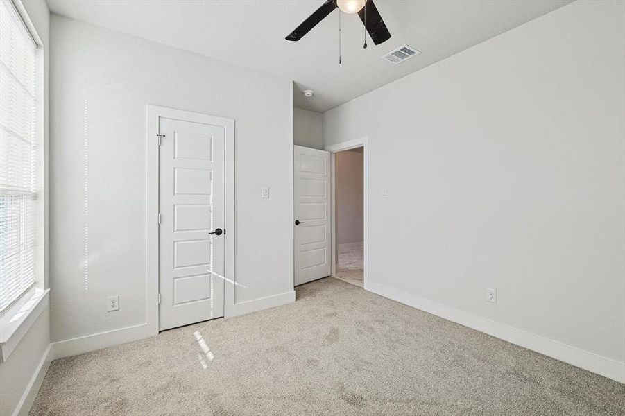 Unfurnished bedroom featuring multiple windows, light colored carpet, and ceiling fan