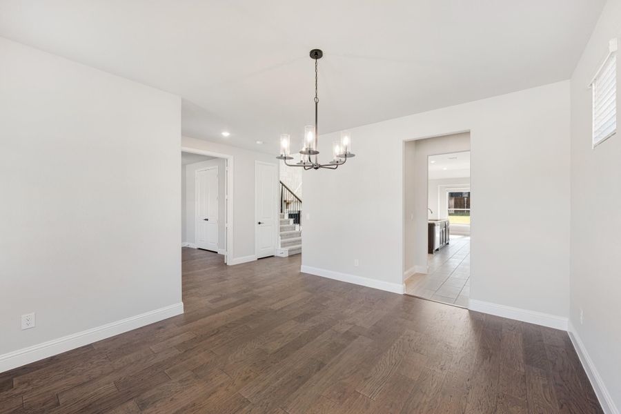 Empty dining room with dark hardwood floors, white walls, and a chandelier overhead Empty dining room with dark hardwood floors, white walls, and a chandelier overhead