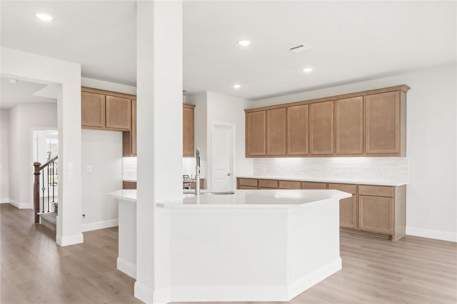 Open kitchen with white island, tan wood cabinets, tile backsplash, and light hardwood floors