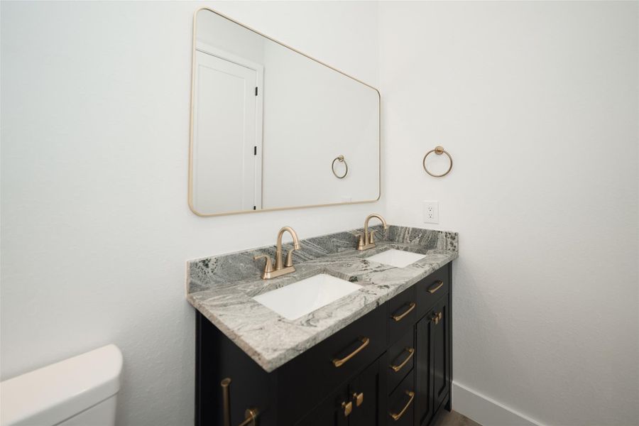 This bathroom features a modern design with a dual-sink vanity, granite countertops, and sleek fixtures.