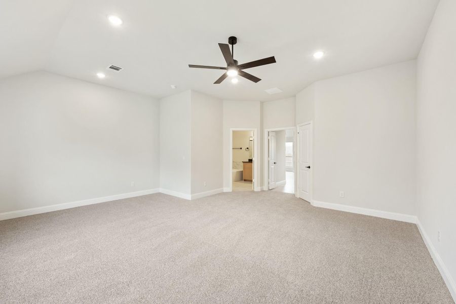 Empty bedroom with gray carpet, ceiling fan, and doorway leading to ensuite bathroom