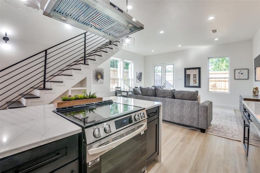 Kitchen with light stone countertops, light hardwood / wood-style flooring, extractor fan, and stainless steel electric range oven