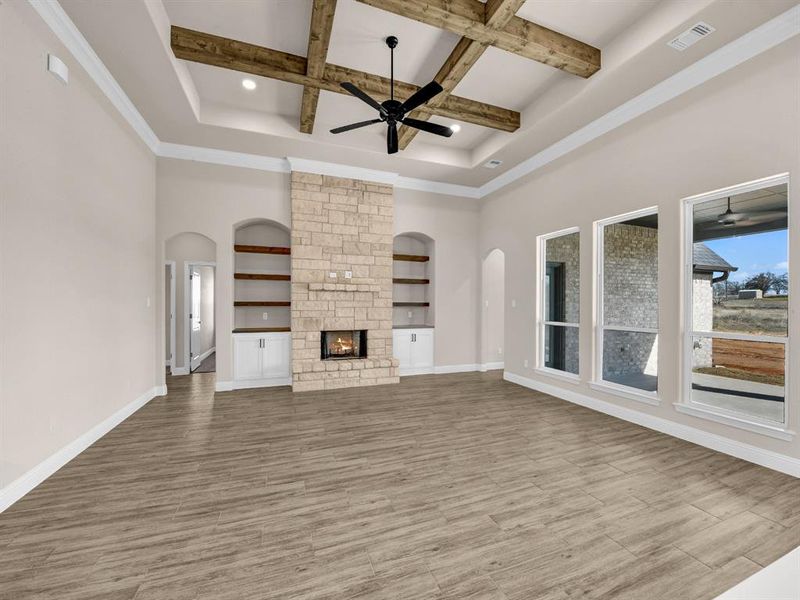 Unfurnished living room featuring coffered ceiling, a high ceiling, beamed ceiling, and a stone fireplace