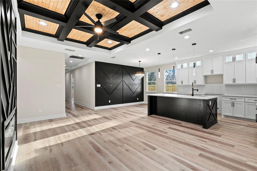 Kitchen featuring coffered ceiling, pendant lighting, a center island with sink, light hardwood / wood-style flooring, and white cabinets