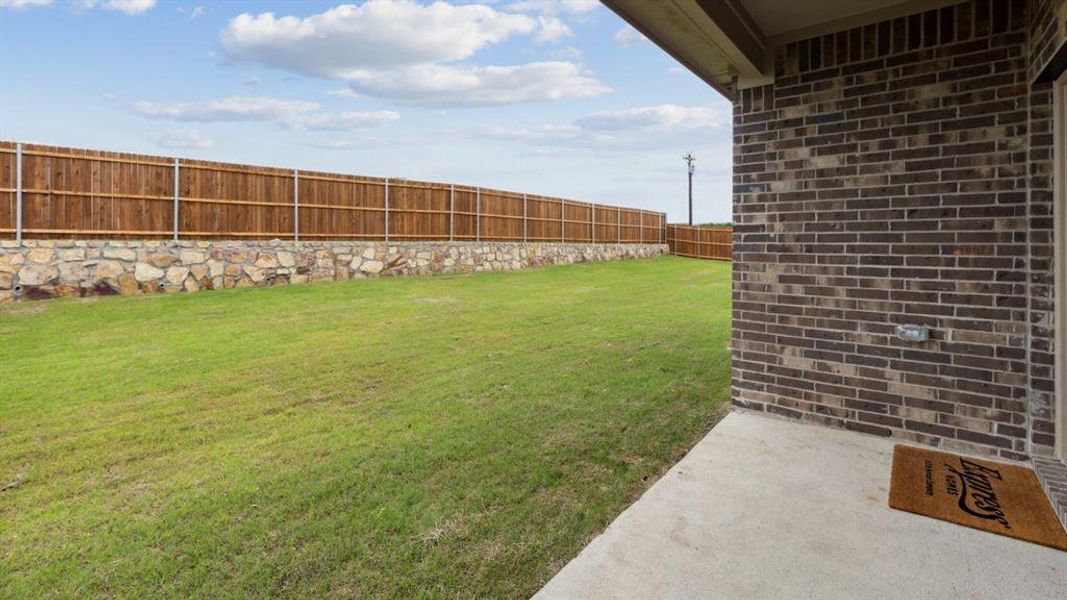 Expansive backyard featuring a manicured lawn, a natural stone retaining wall, and a wood privacy fence