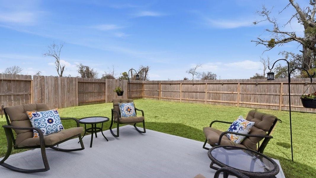 This photo showcases a spacious backyard with a well-maintained lawn, enclosed fence. There's a cozy patio area featuring comfortable seating with cushions and small tables, making it perfect for outdoor relaxation and entertaining.