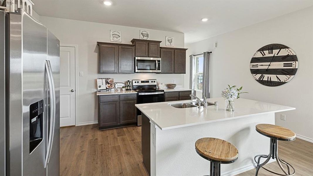 The kitchen features dark wood cabinetry, stainless steel appliances, and a central island with a sink and white countertop