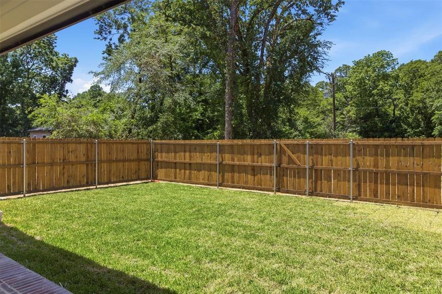 Spacious backyard featuring a manicured lawn and a privacy fence with a gate