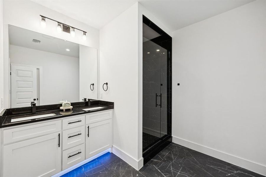 Full bathroom with double vanity, a shower stall, and dark marble finish floors