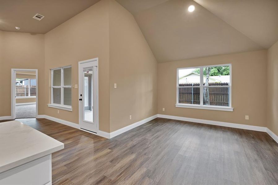 Unfurnished living room with baseboards, wood finished floors, visible vents, and high vaulted ceiling Unfurnished living room with baseboards, wood finished floors, visible vents, and high vaulted ceiling