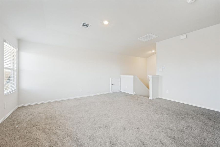 Spacious carpeted room featuring white walls, recessed lighting, and a window with horizontal blinds Spacious carpeted room featuring white walls, recessed lighting, and a window with horizontal blinds