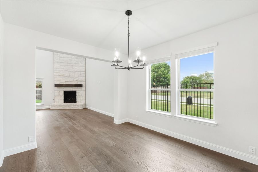 Open dining and living area with hardwood floors, stone fireplace, and black chandelier near large windows Open dining and living area with hardwood floors, stone fireplace, and black chandelier near large windows