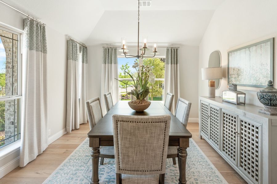 Formal dining room with dark wood table, upholstered chairs, chandelier, and vaulted ceiling