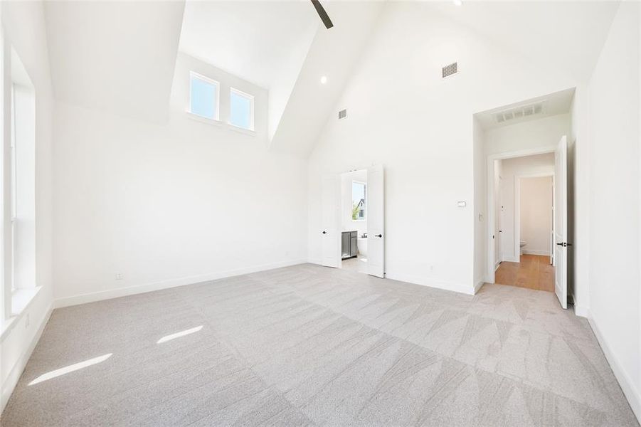 Unfurnished bedroom featuring high vaulted ceiling, light carpet, ensuite bathroom, ceiling fan, and recessed lighting