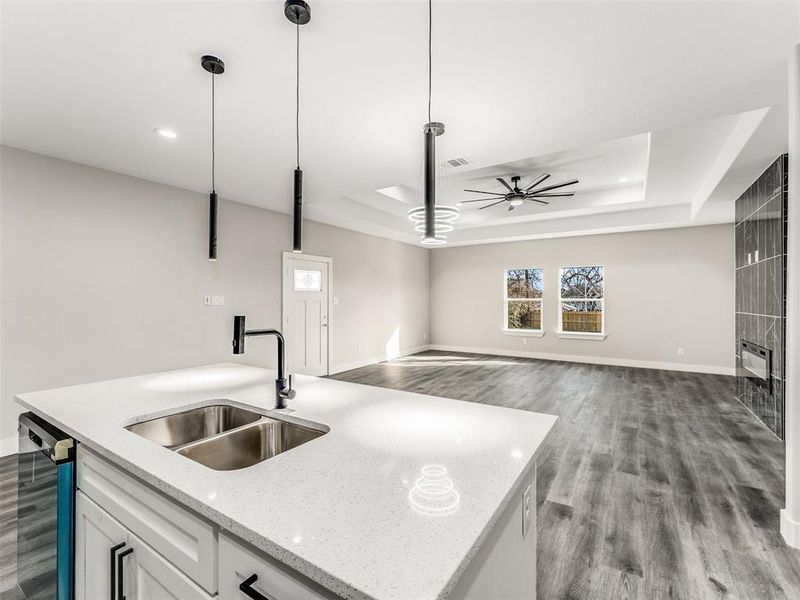 Kitchen featuring a center island with sink, white cabinets, sink, a tray ceiling, and decorative light fixtures