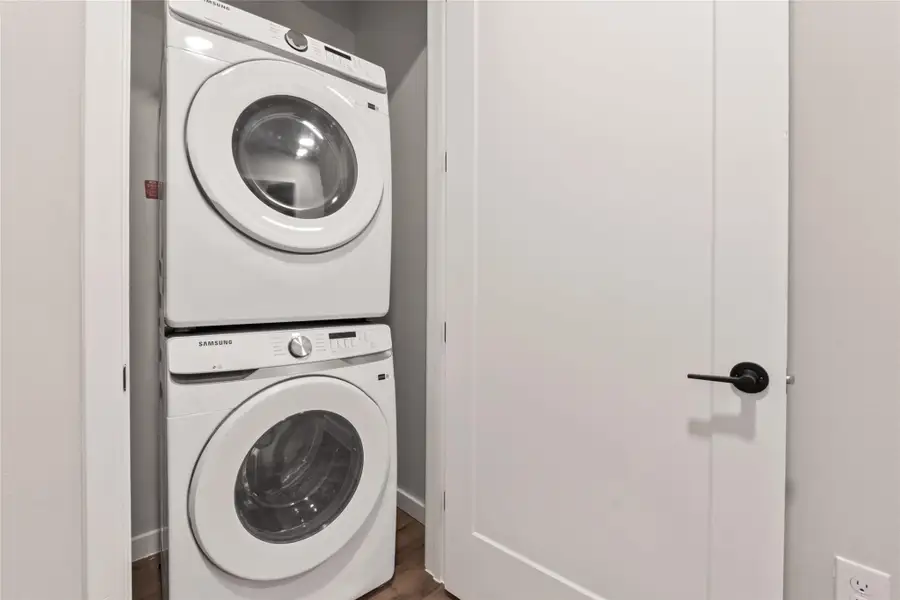 Laundry area featuring stacked washer / drying machine and dark wood-type flooring