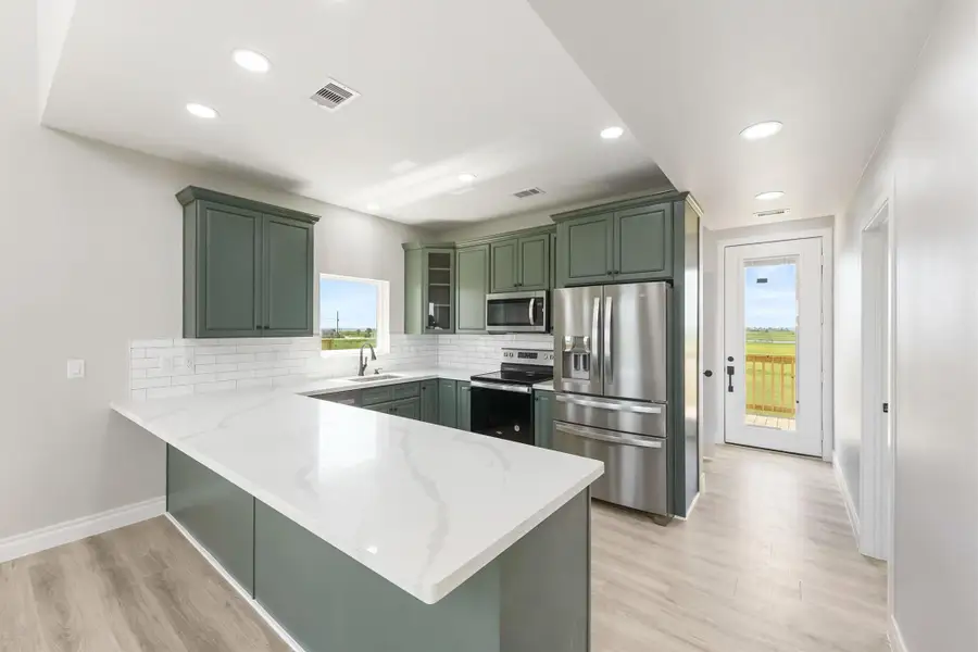 This modern kitchen features sleek green cabinetry, stainless steel appliances, and a spacious white marble countertop. It has a bright, open layout with a door leading to a deck, offering a view of the outdoors. This modern kitchen features sleek green cabinetry, stainless steel appliances, and a spacious white marble countertop. It has a bright, open layout with a door leading to a deck, offering a view of the outdoors.