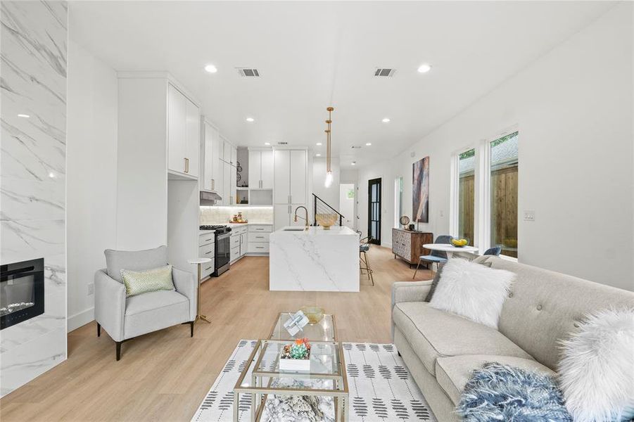 Living room with a high end fireplace, light wood-style floors, visible vents, and recessed lighting