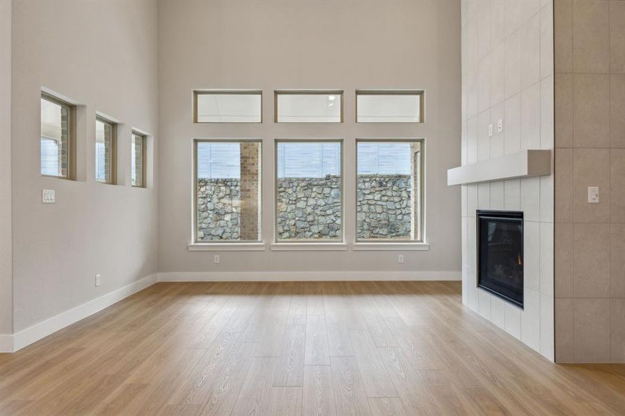 Unfurnished living room with light wood finished floors, a tile fireplace, and a towering ceiling