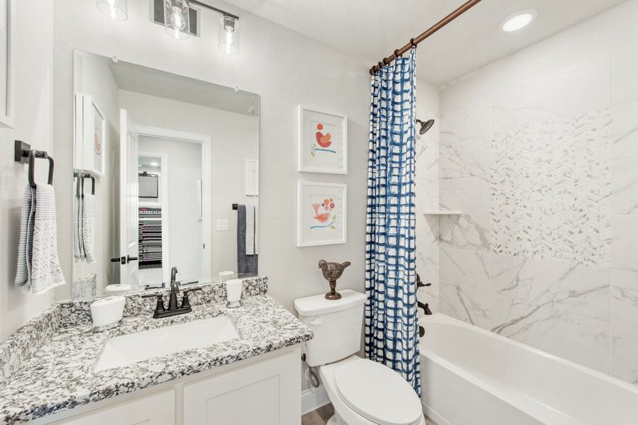 Full bathroom with granite vanity, white cabinets, and tub-shower combo with marble tile surround