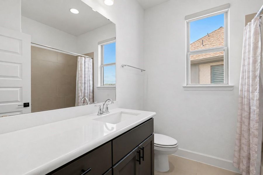 Located just between the secondary bedrooms, this full bathroom features natural light, a spacious quartz countertop, dark cabinets, a spacious tub/shower combo, and a large mirror.