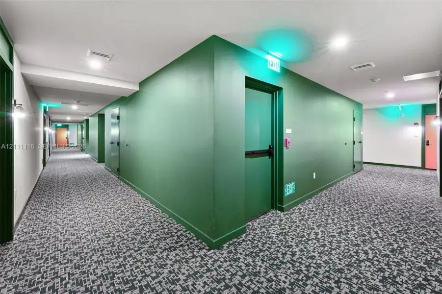 Interior corridor featuring patterned wall-to-wall carpeting, recessed ceiling lighting, and solid-core metal doors