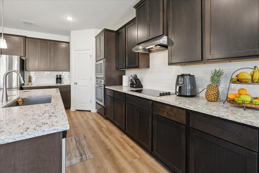 Kitchen featuring appliances with stainless steel finishes, light wood-type flooring, backsplash, sink, and decorative light fixtures